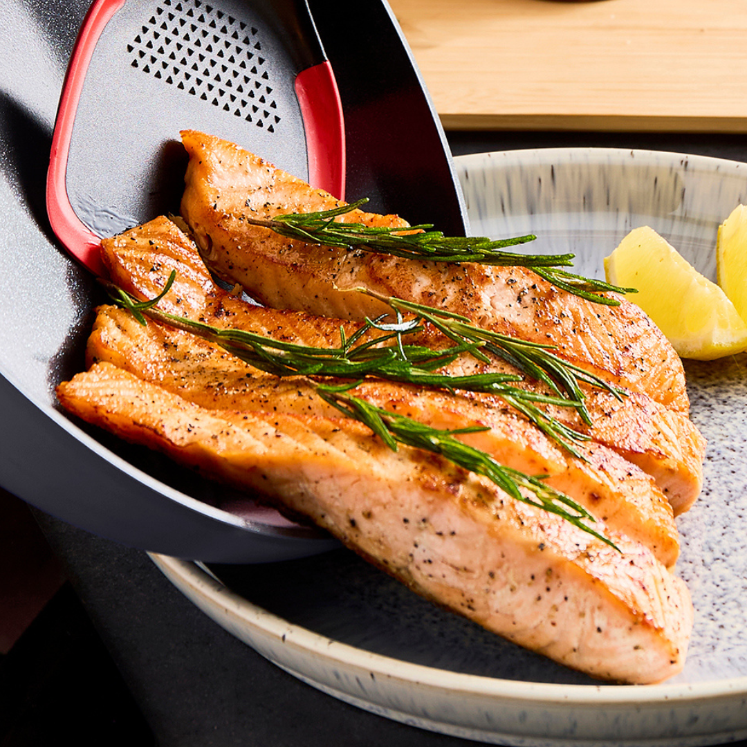 Grilled salmon fillets with rosemary on a plate, served with lemon wedges.