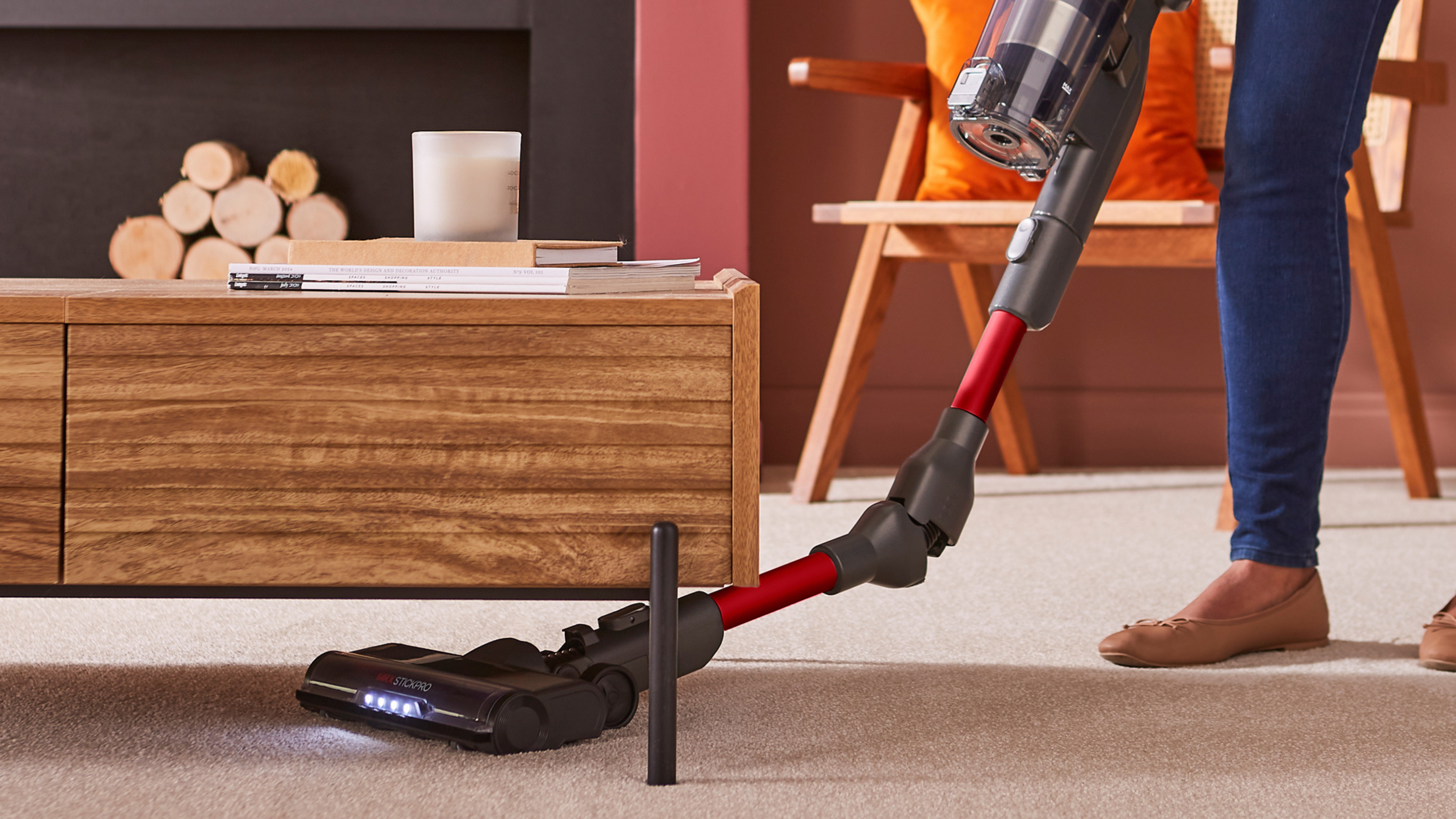Person using a cordless vacuum cleaner on a carpeted floor in a living room.